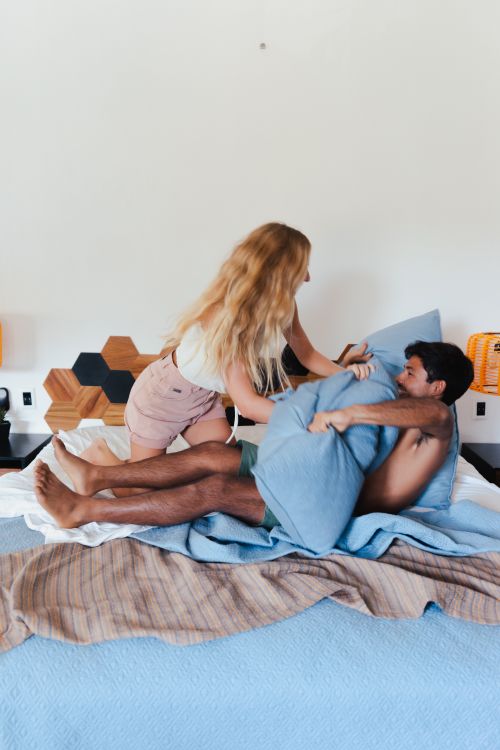 Playful couple enjoying a pillow fight in a cozy bedroom, representing the lighter, exploratory side of fetish psychology