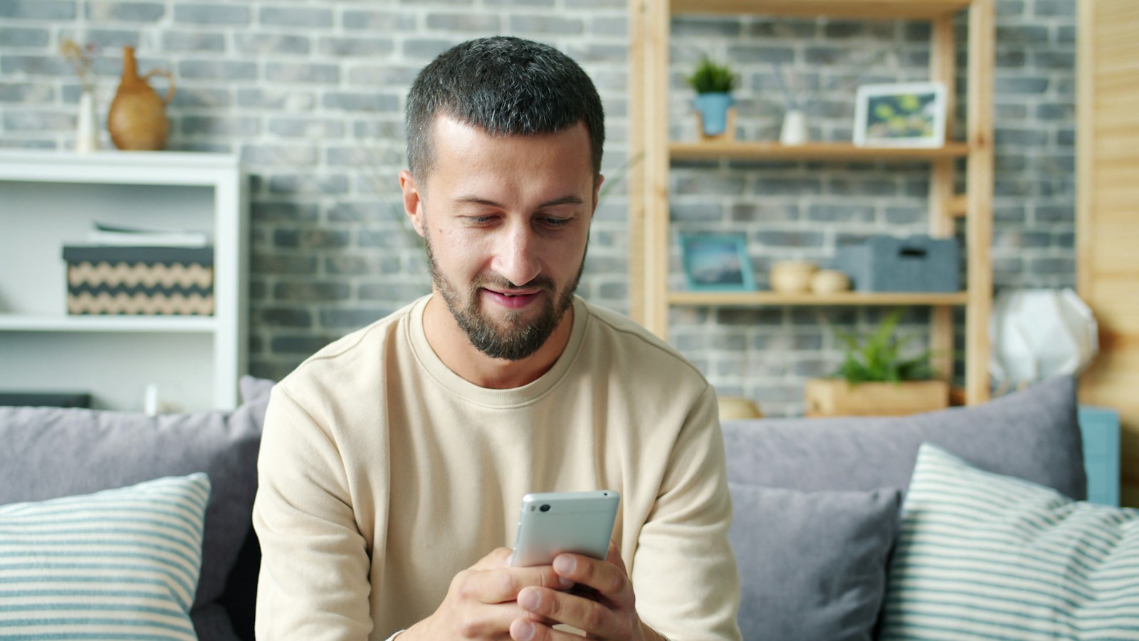 A man sitting on a couch looking at his smartphone, waiting on a reply to a text message